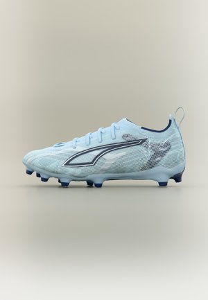 Adidași de fotbal de culoare albastru deschis cu crampoane de culoare albastru închis și un logo stilizat gri pe lateral, pe un fundal bej simplu.