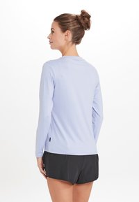 Lys blå langærmet skjorte med rund halsudskæring og sideslits, parret med sorte shorts. Glat tekstur, minimal branding.