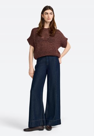 Maglione a maglia bordeaux con vestibilità ampia, abbinato a pantaloni in denim scuro a gamba larga. L'outfit presenta un motivo testurizzato e cuciture a contrasto.