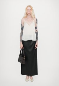 Camisol din mătase albă transparentă, cu detalii fine din dantelă, asortat cu o fustă lungă din piele neagră. Accesorii cu o geantă mică maro și pantofi plată crem.