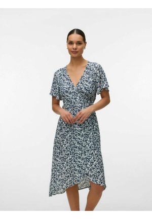 Mujer de pie que lleva un vestido cruzado hasta la rodilla en azul marino con flores blancas, con mangas cortas y vuelo y un escote en V.