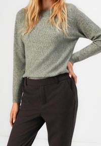 Pull vert en tricot avec un col rond, des poignets côtelés et une coupe décontractée, associé à un pantalon marron foncé tailleur avec poches latérales.