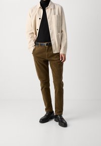 Beige cotton jacket with black buttons, black turtleneck, brown corduroy pants, and black loafers with decorative hardware.
