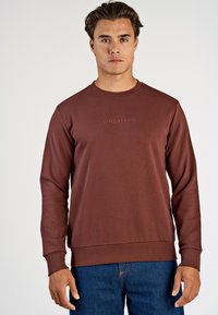 Vinröd sweatshirt med långa ärmar, ribbad halsringning och mudd. Har en diskret "LINDBERGH"-logotyp över bröstet. Varmt, strukturerat tyg.