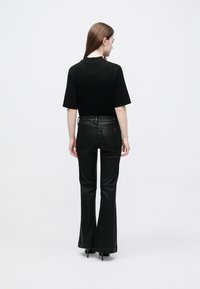 Fekete bordázott rövid ujjú felső, fekete testhezálló, enyhén bővülő nadrággal párosítva, sima textúrával és egyszerű dizájnnal.