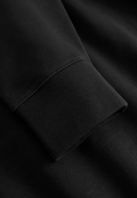 Tissu de sweat-shirt noir avec une surface texturée et un détail de bord-côte côtelé. La manche est pliée pour révéler la couture.