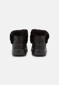 Botas de tobillo de imitación de piel de borrego negro con un exterior de cuero suave y cuello acolchado. Presentan una suela de goma y un logotipo grabado en el talón.