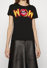 Černé bavlněné tričko s červenou a žlutou grafikou "WOW" se stylizovaným ústy. Krátké rukávy a střih s kulatým výstřihem.