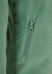 Tessuto di giacca in pile verde con una vista ravvicinata di una tasca con zip, caratterizzata da una zip in plastica e una consistenza liscia e morbida.
