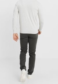 Helles graues Sweatshirt und dunkelgraue Hose, beide tailliert. Die Hose hat eine glatte Textur. Weiße Sneakers sind am unteren Rand sichtbar.