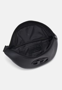 Czarna skórzana saszetka o zaokrąglonym kształcie, z zamkiem błyskawicznym i teksturowanym wnętrzem z delikatnym wzorem logo. Na froncie wyróżnia się duża metalowa ozdoba z logo.