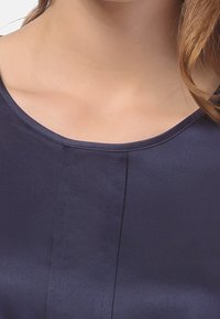 Chemisier en soie bleu marine avec un col rond et une texture lisse. Présente des détails de couture verticaux sur le devant.