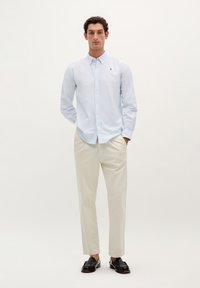 Camicia blu chiaro con un motivo sottile, maniche lunghe e colletto classico, abbinata a pantaloni crema e mocassini neri.
