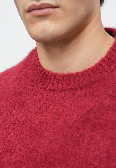 Κόκκινο πλεκτό πουλόβερ με ριγέ στρογγυλή λαιμόκοψη, που έχει απαλή και χνουδωτή υφή και ελαφρώς χαλαρή εφαρμογή, επιδεικνύοντας μια πλούσια, ζεστή απόχρωση.