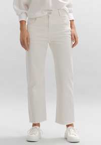 Jeans blancos de corte recto con dobladillo deshilachado, cinco bolsillos y cierre con botón de metal, combinados con zapatillas blancas. Textura de tela suave.