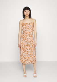 Vestido midi castanho com padrão e alças finas; apresenta desenhos abstratos brancos. O tecido suave cai até a altura da meia-perna. Sandálias brancas.