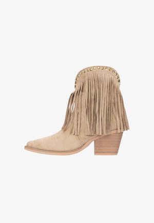Bottine en daim beige avec des franges, des clous dorés sur le bord supérieur et un talon bloc empilé en bois.