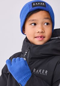 Kék kötött sapka fekete címkével és kék kesztyű, mindkettő szövetből készült. Egy fekete dzseki cipzárral és logóval, magas gallérral.