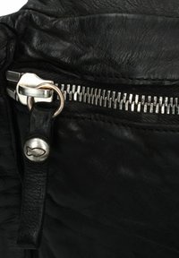 Angolo di borsa in pelle nera con zip argentata, hardware metallico a forma di pesce e superficie texturizzata. Tirazip attaccato a una tracolla in pelle.