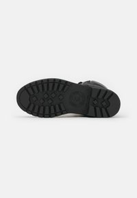Bota de cuero negra con una suela de goma texturizada que presenta un patrón de tacos, herrajes metálicos y un cierre de cremallera en el lateral.