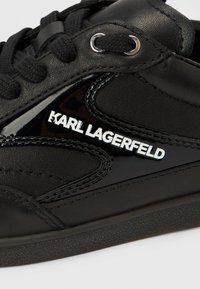 Schwarzer Ledersneaker mit glänzenden Akzenten, strukturierten Seiten, Schnürdesign und einem silbernen "KARL LAGERFELD"-Logo an der Seite.