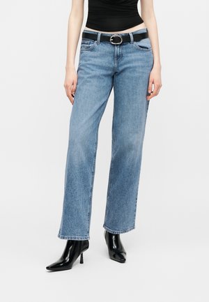 Γυναίκα που φοράει ανοιχτό μπλε τζιν με ίσια γραμμή, μαύρη ζώνη με ασημένια πόρπη, μαύρο αμάνικο τοπ και μαύρα μυτερά μποτάκια με τακούνι.