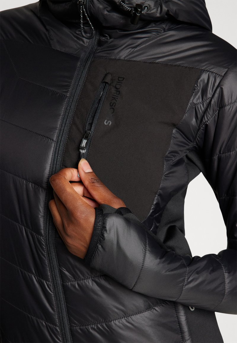 Schwarze, gepolsterte Jacke mit glatter Oberfläche, ausgestattet mit einer Reißverschluss-Brusttasche, elastischen Bündchen und Kapuze, die kontrastierende strukturierte Paneeldetails zeigt.