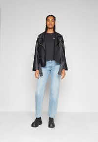 Veste en cuir motard noire avec des accessoires en argent, associée à un haut noir et un jean droit bleu clair. Des bottes à plateforme noires complètent la tenue.