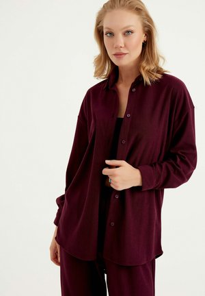 Maroon button-up shirt with ribbed texture, long sleeves, and a relaxed fit, paired with a black top and matching pants.