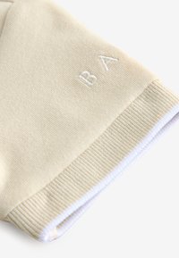 Ljust beige sweatshirtmanschett med ribbad struktur. Har en vit broderad "BA" logotyp nära kanten. Mjuk tyg, avslappnad stil.