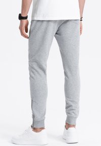 Grey sweatpants with a slim fit, made of soft material, featuring a zip at the ankle and ribbed cuffs, paired with white sneakers.