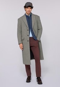 Grå ullrock med sned krage, i kombination med en marinblå vadderad väst, blå skjorta, vinröda byxor och mörkbruna loafers.