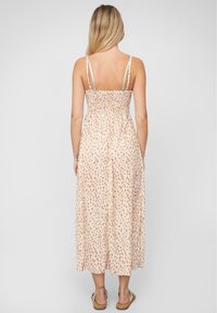 Robe maxi en tissu doux pêche avec un motif à pois marron ; corsage ajusté avec détail de smocks ; fines bretelles réglables ; silhouette fluide.