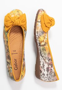 Płaskie buty z fakturowaną, wielokolorową cholewką z żółtymi akcentami i kokardą. Brązowa podeszwa z perforowaną wkładką dla komfortu. Widoczne logo Gabor.