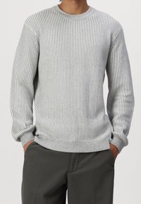Pull tricot gris à rayures avec un col rond, texture côtelée et manches longues, associé à un pantalon foncé.
