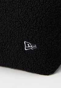 Μαύρο φλις υλικό με υφή, αφράτη επιφάνεια. Διαθέτει ένα λευκό κεντημένο λογότυπο από τη μία πλευρά, προσθέτοντας λεπτομέρεια στο σχέδιο.