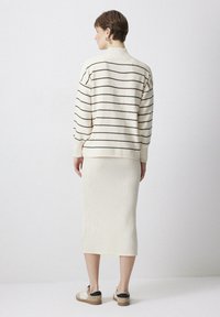 Krémový pruhovaný sveter s rebrovanou textúrou a vysokým golierom, skombinovaný s rebrovanou krémovou midi sukňou a ležérnymi svetlými topánkami.