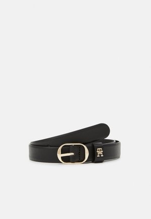 Ceinture en cuir noir roulée avec boucle ovale dorée et petit logo doré sur la passants de ceinture, présentée sur fond blanc.