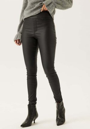 Svarta fusk läder skinny byxor med hög midja, framfickor och en slät textur, kombinerade med svarta spetsiga ankelstövlar och en grå tröja.