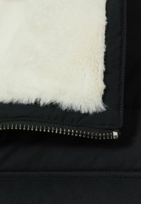 Jachetă neagră cu un strat interior moale din blană de culoare crem. Prezintă un fermoar argintiu în partea de jos și o textură exterioară netedă, mate.