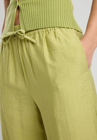 Vihreät pellavasekoitekankaiset housut, joissa on rento leikkaus, elastinen vyötärö, sivutaskut ja rypytetty pinta.
