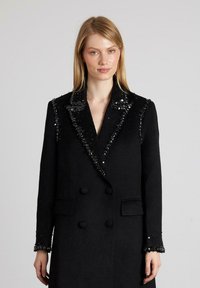 Abrigo de lana negro con diseño de doble botonadura, cuello y puños adornados con lentejuelas, solapas con muesca y bolsillos frontales. Texturizado y estructurado.