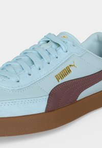 Ανοιχτό μπλε αθλητικό παπούτσι Puma με καφέ πλευρική ρίγα, χρυσό λογότυπο Puma, μπλε κορδόνια και καφέ καουτσούκ σόλα σε λευκό φόντο.
