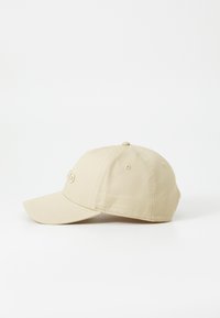 Beige bomuldsbaseballcap med en buet skygge, broderet logo på fronten og en knap på toppen. Klassisk tætsiddende design med struktureret stof.