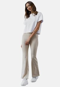 Biały, krótki t-shirt połączony z beżowymi spodniami w dzwony, charakteryzującymi się gładką fakturą i swobodnym krojem. Stylizowany z białymi sneakerami.