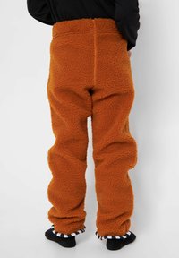 Rust orange fleecebukser med et blødt, tekstureret stof, høj talje og afslappet pasform, med sort og hvidstribede sokkeaccenter ved anklerne.