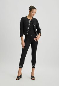 Jachetă din denim negru cu broderie florală, asociată cu blugi skinny negri cu margini brodate și sandale cu toc deschise la vârf.