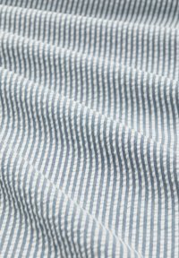 Tissu à rayures verticales bleu clair et blanc avec des plis doux et une surface texturée.