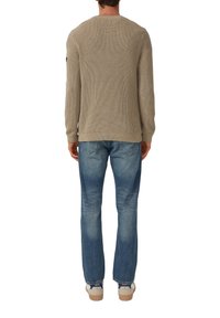 Strickpullover in hellbeige mit gerippter Textur, kombiniert mit blauen Straight-Leg-Jeans. Sneaker mit kontrastierenden Details runden das Outfit ab.
