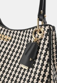 Borsa a tracolla intrecciata in bianco e nero con dettagli in oro, che presenta un'etichetta in pelle sospesa e un logo del marchio ben visibile. Texture liscia, forma strutturata.